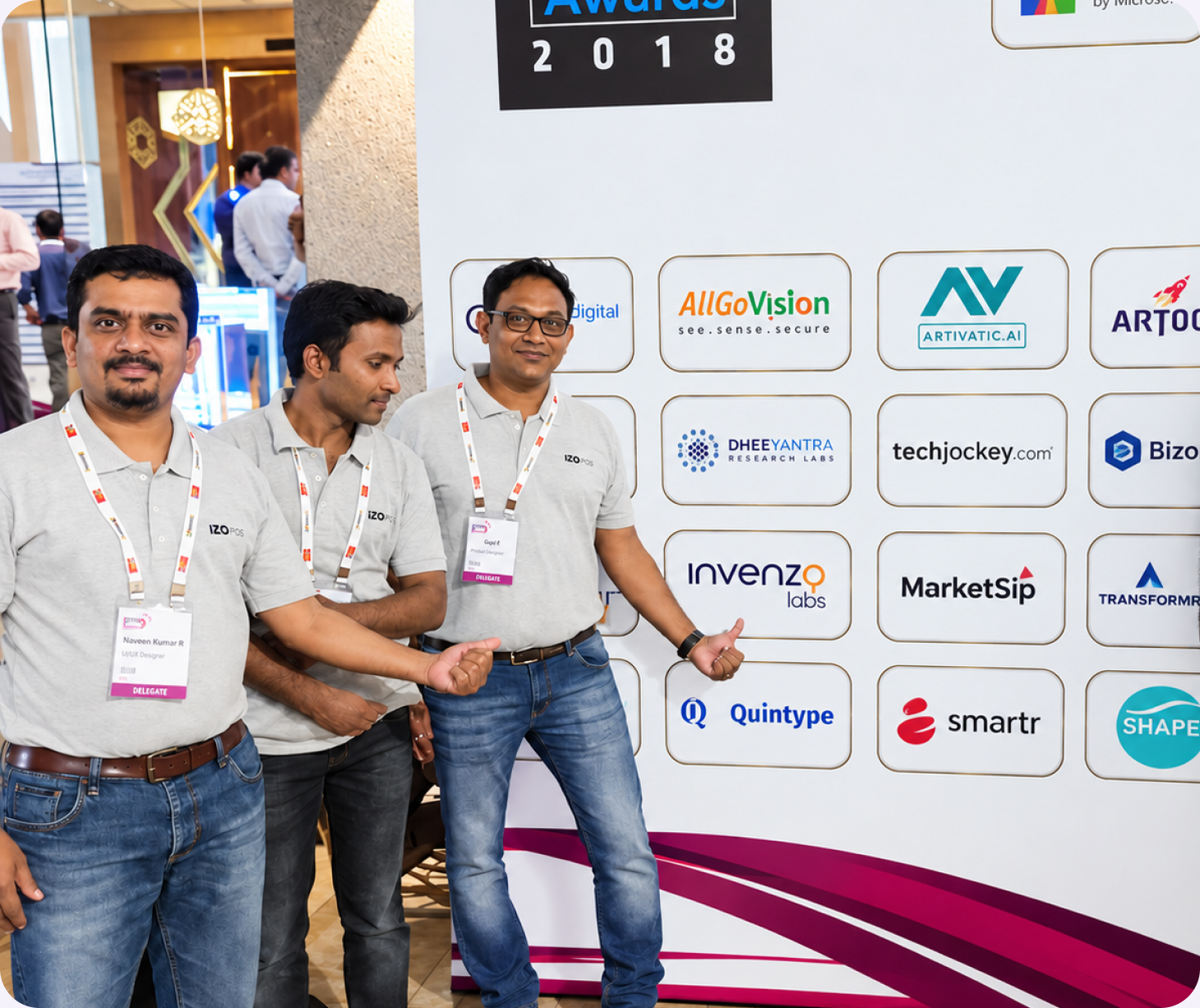 Three Invenzo Labs team members in event polos standing at a sponsor wall, with the Invenzo Labs logo visible among the other exhibitor logos.