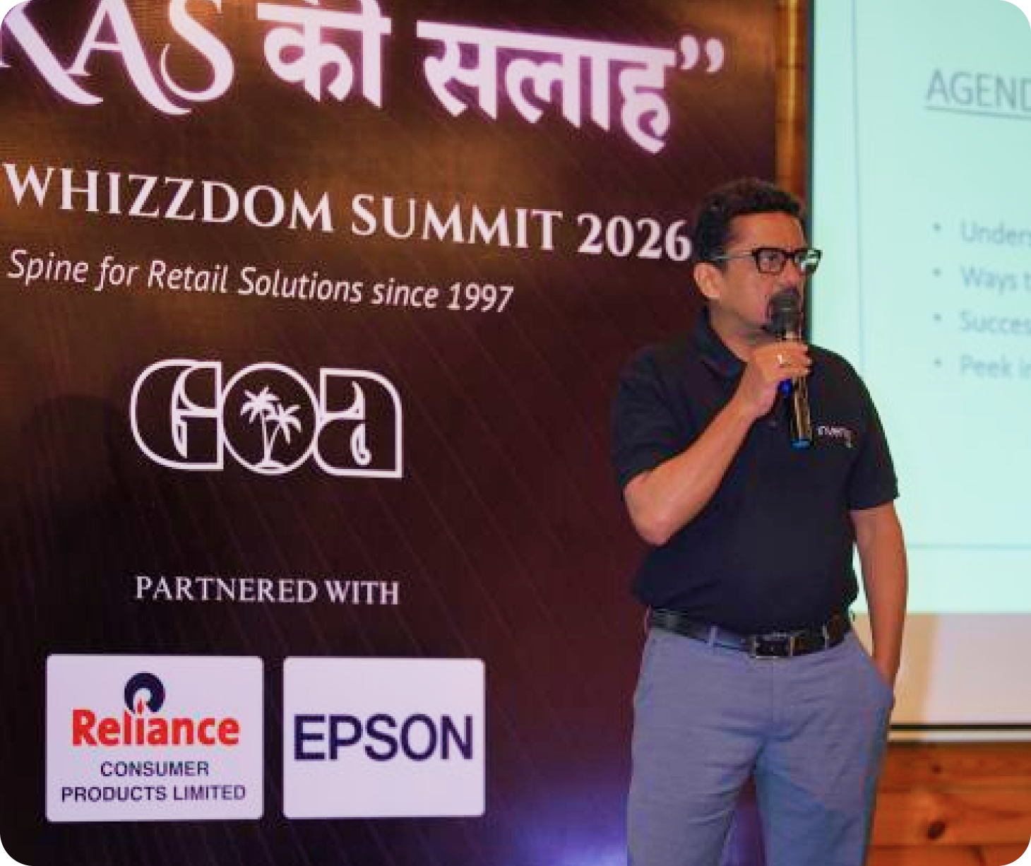 Raj Gopal on stage at the RETAILWHIZZDOM Summit 2026, speaking beside the event backdrop and agenda slide.